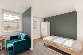 A studio room in 34 Park Street, partially partitioned by a wall. The left hand side of the room is a living room with a sofa and the right hand side of the room has a double bed and wardrobe in the far corner.